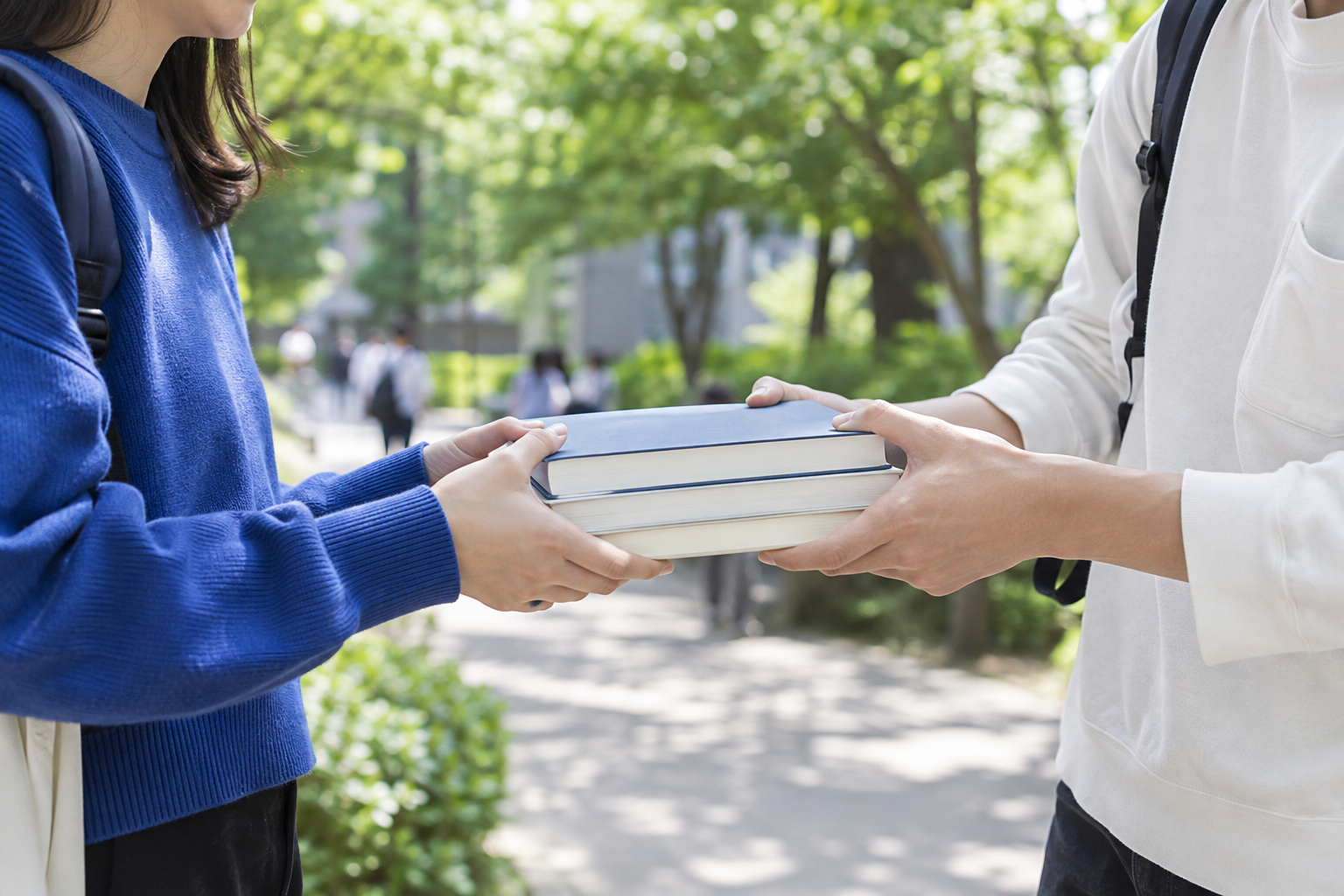 キャンパスで教科書を手渡す大学生のイメージ